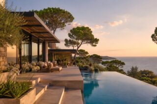 Terrace of a contemporary villa at dusk, with an infinity pool and umbrella pines above the sea