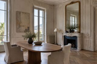 Salle à manger aux murs moulurés, table ovale en bois, cheminée claire et grand miroir doré